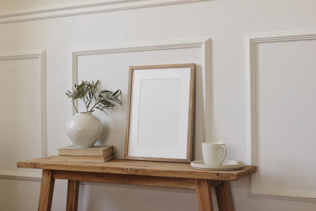 Minimalist Interior Picture Frame Mockup on Wooden Table. Vase Olive Branch, old Books, Coffee Cup still life. Mediterranean Home Decor Scene. Blank Poster Template. Neutral Wall Background, side view