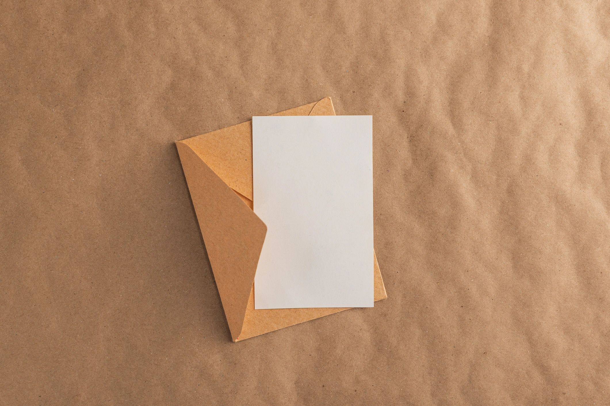 Open brown envelope with blank white card on kraft paper