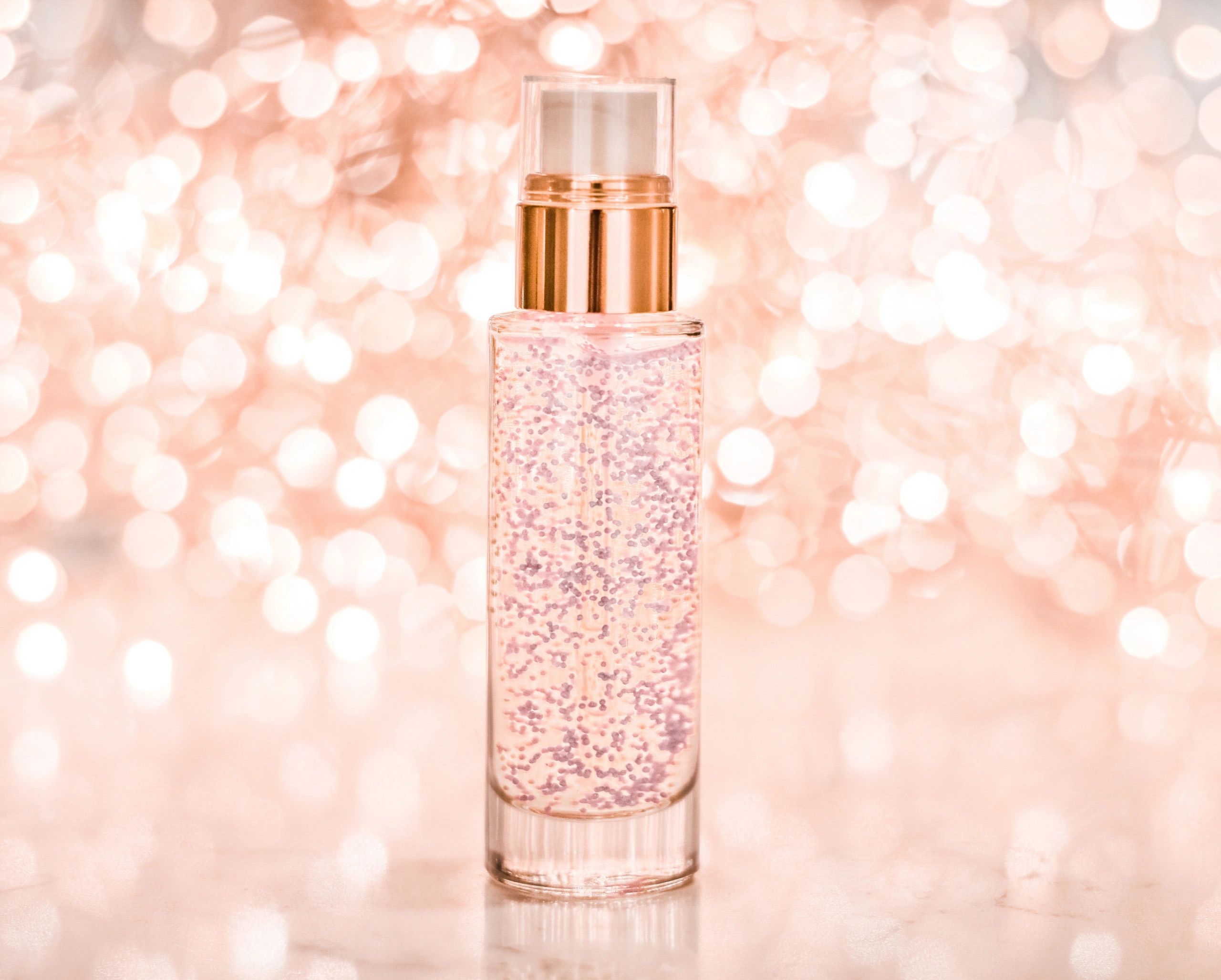 Cosmetic serum bottle with rose gold pump and shimmering liquid on a glowing bokeh background